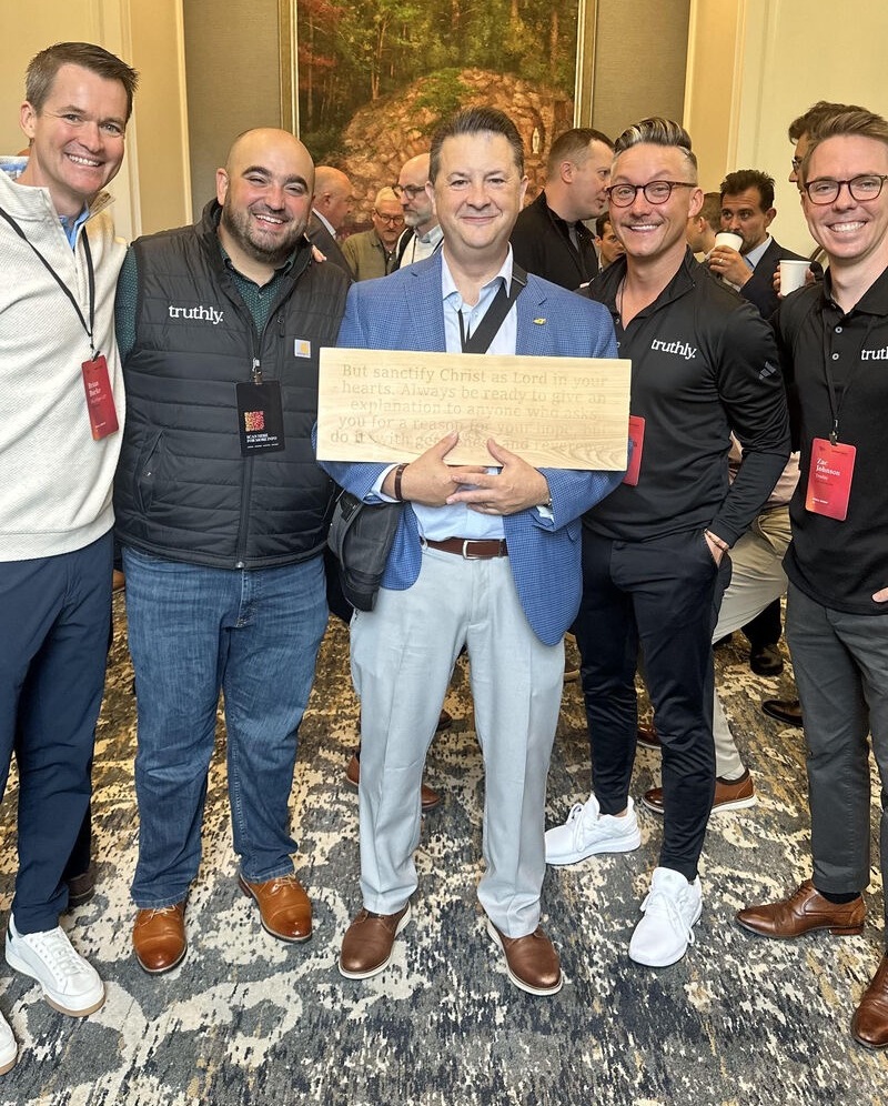 Joe Valentic with the Truthly team holding a Scripture plaque at a Catholic business gathering